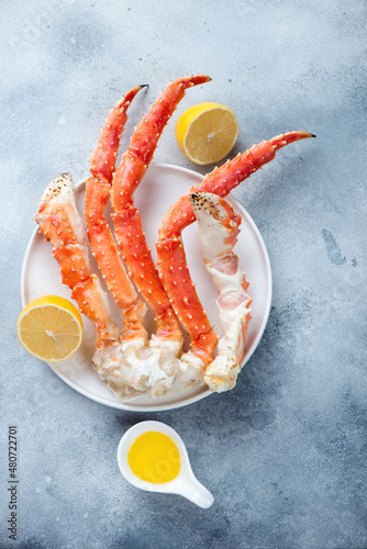 Kamchatka crab claws with lemon and butter, top view on a light-blue stone background, vertical shot