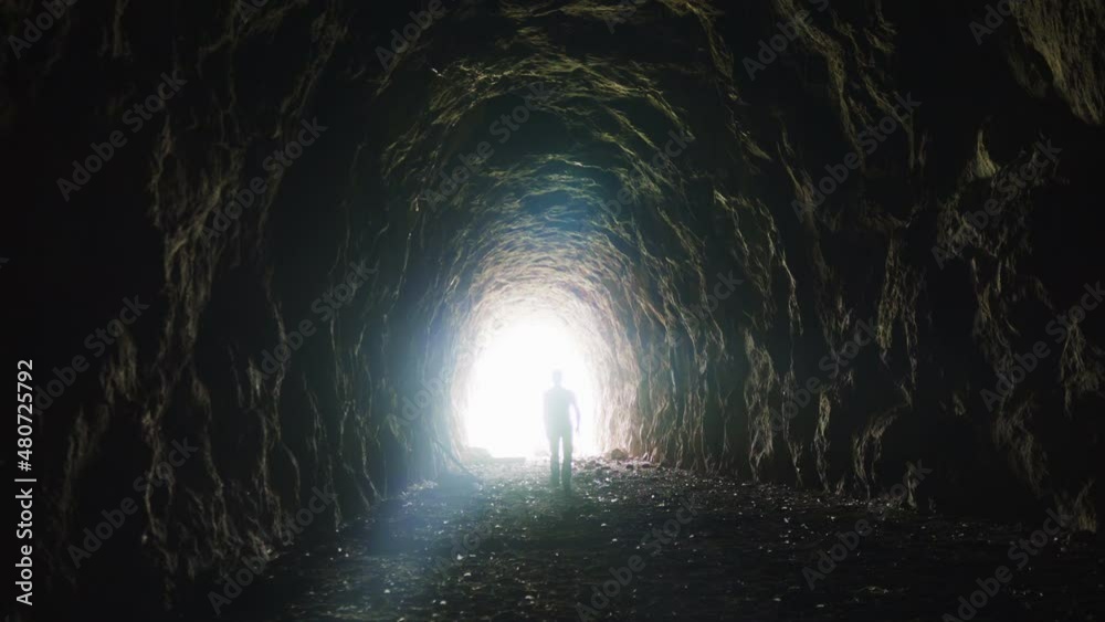 Video 4K of a man walking in an ancient tunnel to the light, a lonely man coming out to meet the divine light, Anotherworldly eerie light at the end of the tunnel