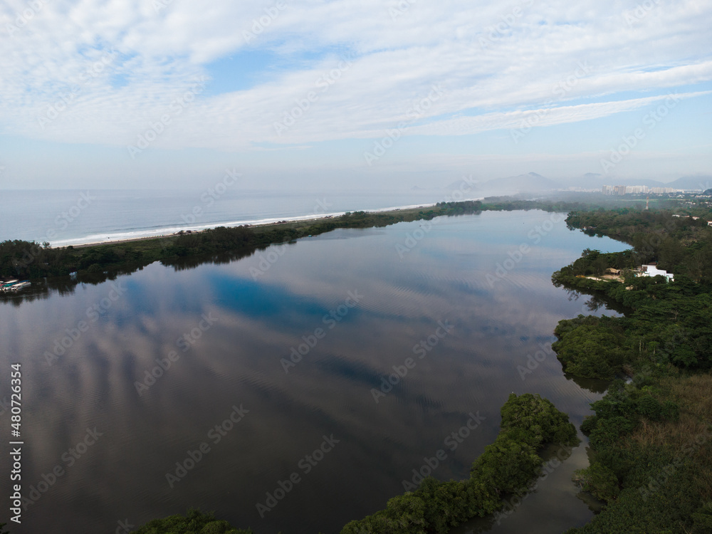 Aerial view of Reserva beach and Marapendi lagoon. In the background, the hills of Recreio dos Bandeirantes, in Rio de Janeiro, Brazil. Dawn. Sunny day with some clouds. Drone photo