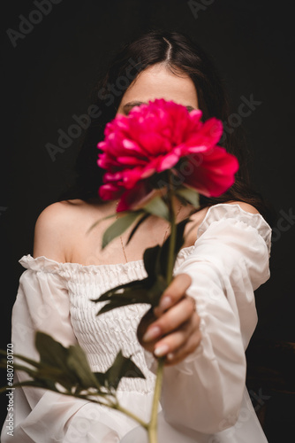 portrait of a young, beautiful and sensual woman with 1 red peony flower in her hands