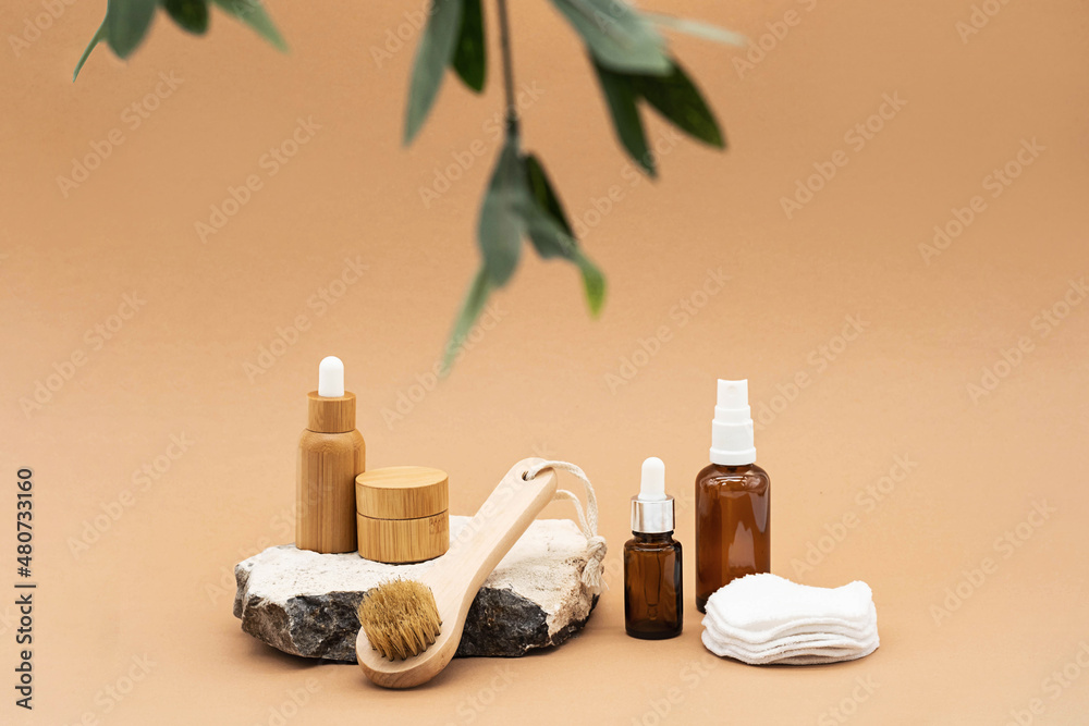 Blank amber glass and bamboo essential oil bottles with pipette, glass spray bottle and bamboo jar on natural stone podium. Organic spa cosmetic beauty product mock up.