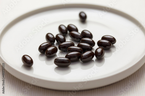白い皿の上の黒色のサプリメントの粒