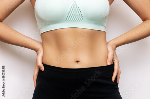 Cropped shot of a young slender woman with toned stomach with abs isolated on a white background. Result of fitness, diet, healthy lifestyle. Female belly after a lot of training. Lines and six-packs © Марина Демешко