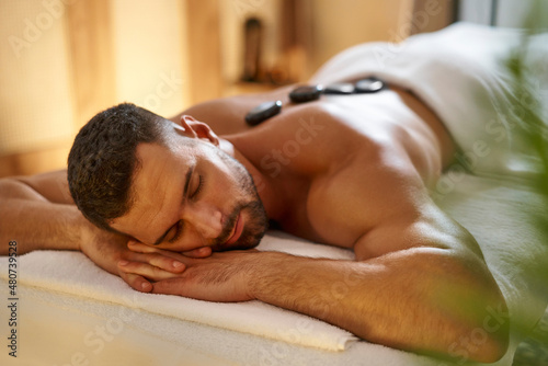 Young man having a hot stone lastone massage at spa photo