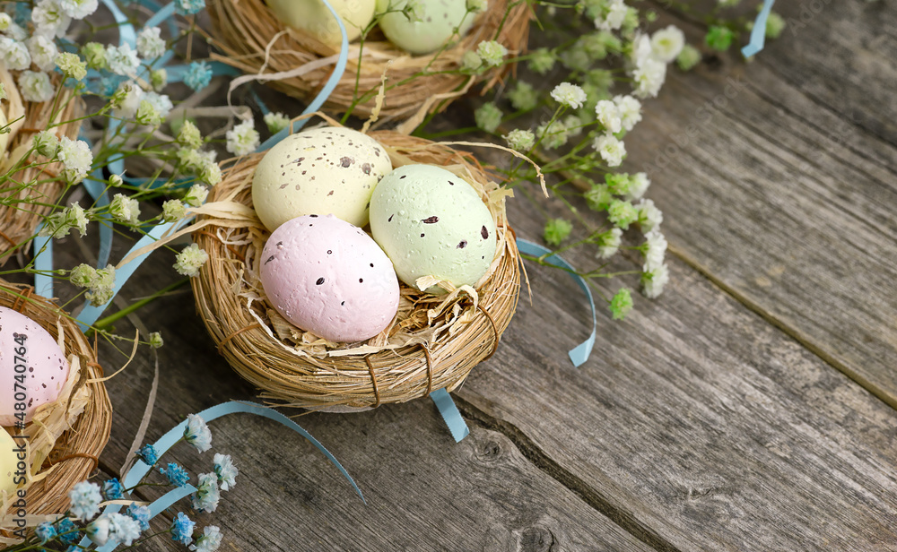 Obraz premium Small quail Easter eggs in a nest of straw on a wooden table. The background is pale blue gypsophila flowers