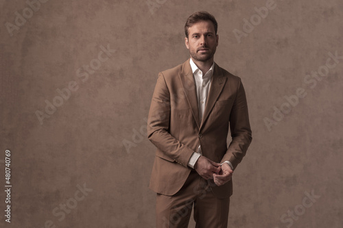 sexy businessman fixing his sleeve and wearing a brown suit