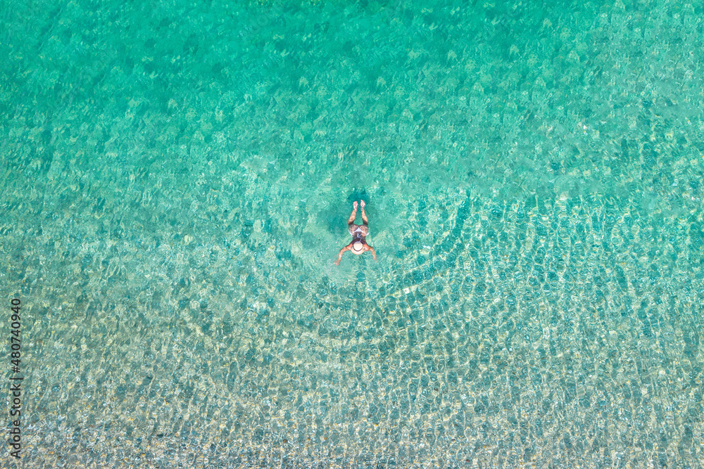 Top, aerial view. Young beautiful woman in a hat and white bikini swimming in sea water on the sand beach. Drone, copter photo. Summer vacation. View from above.