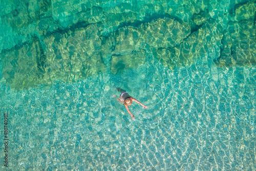 Top  aerial view. Young beautiful woman in white bikini swimming in sea water on the sand beach. Drone  copter photo. Summer vacation. View from above.