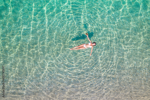 Top, aerial view. Young beautiful woman in white bikini swimming in sea water on the sand beach. Drone, copter photo. Summer vacation. View from above.