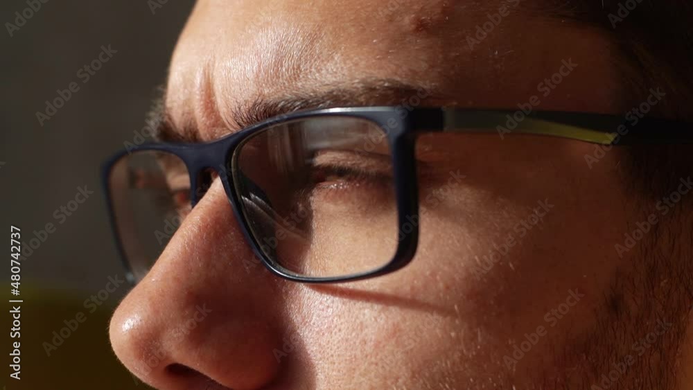 Close-up headshot of overworked young businessman taking off glasses, rubbing dry irritable eyes in dark room. Closeup face of exhausted freelancer male putting on eyeglasses and looking forward.