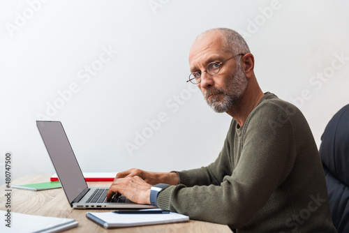 Elderly man working on laptop and looking at camera