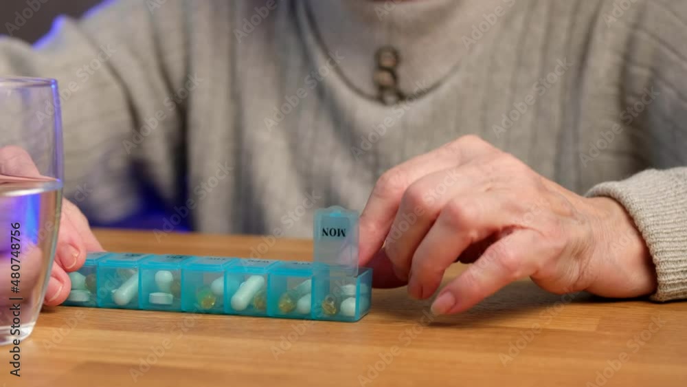 Elderly woman opens pillbox, takes an omega 3 capsule and drinks. Elderly woman opens pillbox, takes an omega 3 capsule and drinks.