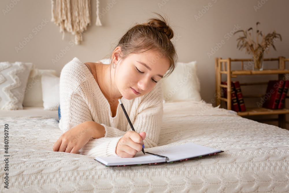 Closeup portrait of a relaxed young girl writing book while lying on the bed Closeup portrait of a relaxed young girl writing book while lying on the bed