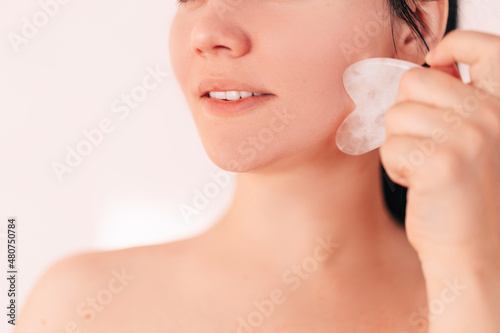 a beautiful brunette girl massages with a gouache scraper. a young woman of European appearance with clean, fresh skin. Jade roller facial massager made of natural stone. Cosmetology. close-up