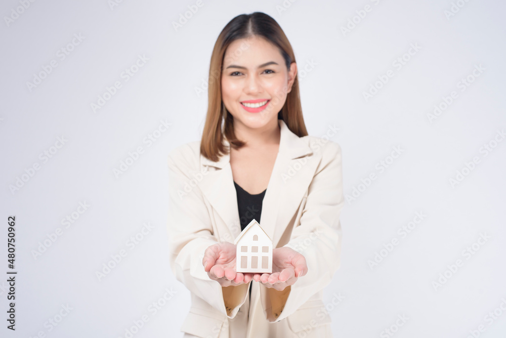 Young beautiful woman in suit holding small model house over white background studio Young beautiful woman in suit holding small model house over white background studio