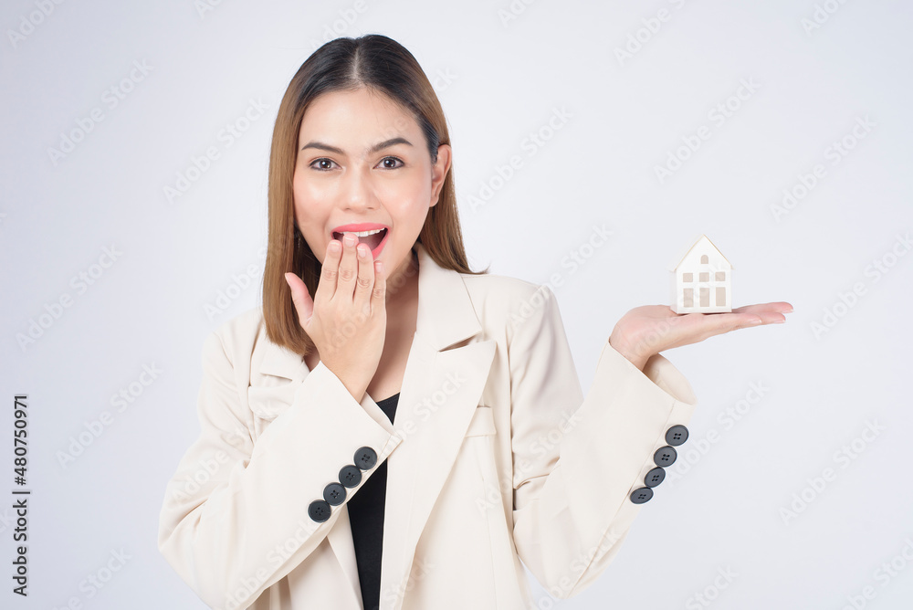 Young beautiful woman in suit holding small model house over white background studio Young beautiful woman in suit holding small model house over white background studio