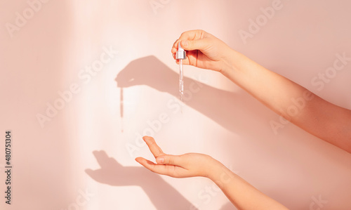 The hands of a young girl with a drop of serum or hyaluronic acid from a pipette on a background. beautiful shade from the sun. Collagen serum drips from the hands of a beautiful woman. photo