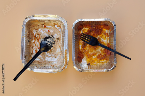 Two empty aluminum containers after lunch top view. Food  containers with disposable plastic utensils. Dirty disposable tableware after eating on a beige background.