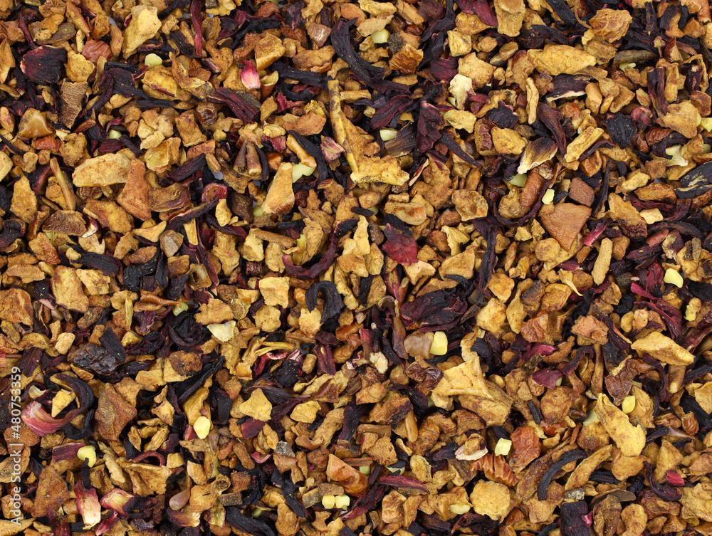 Red fruit tea with nut pieces and hibiscus leaves background. Aromatic tea made from fruits, spices and nuts. Dry pieces of apple, berries, spices and pieces of nuts close-up. Delicious drink.