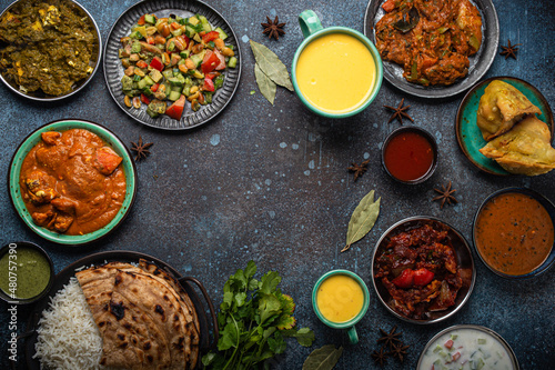 Indian ethnic food buffet on concrete table from above: curry, samosa, rice biryani, dal, paneer, chapatti, naan, chicken tikka masala, mango lassi, dishes of India for dinner background copy space