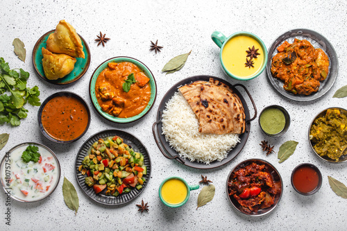 Indian ethnic food buffet on white concrete table from above: curry, samosa, rice biryani, dal, paneer, chapatti, naan, chicken tikka masala, mango lassi, dishes of India for dinner background