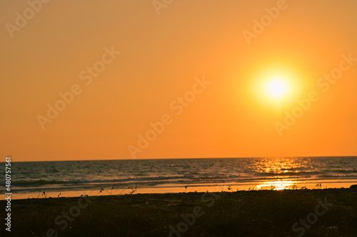 Summer sunset view on the beach. Beautiful blazing sunset landscape and orange sky above it with sun reflection on waves.