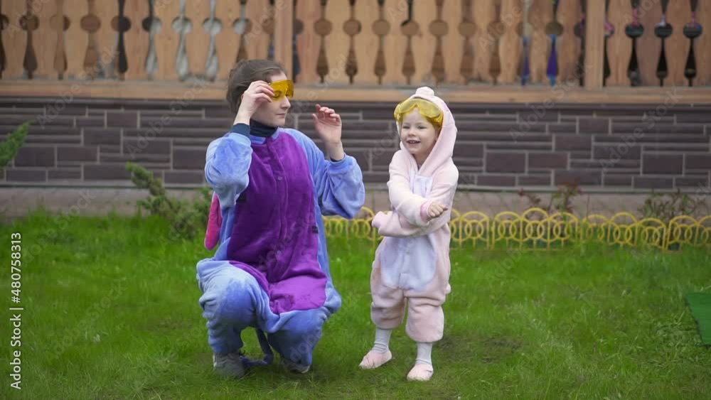 crazy dance girl and woman in kigurumi pajamas. Two sisters have fun. lovely mom, dancing, relaxing clothes, cosplay, pajamas, daughter. Close-up family enjoy music and party on front lawn. outdoor