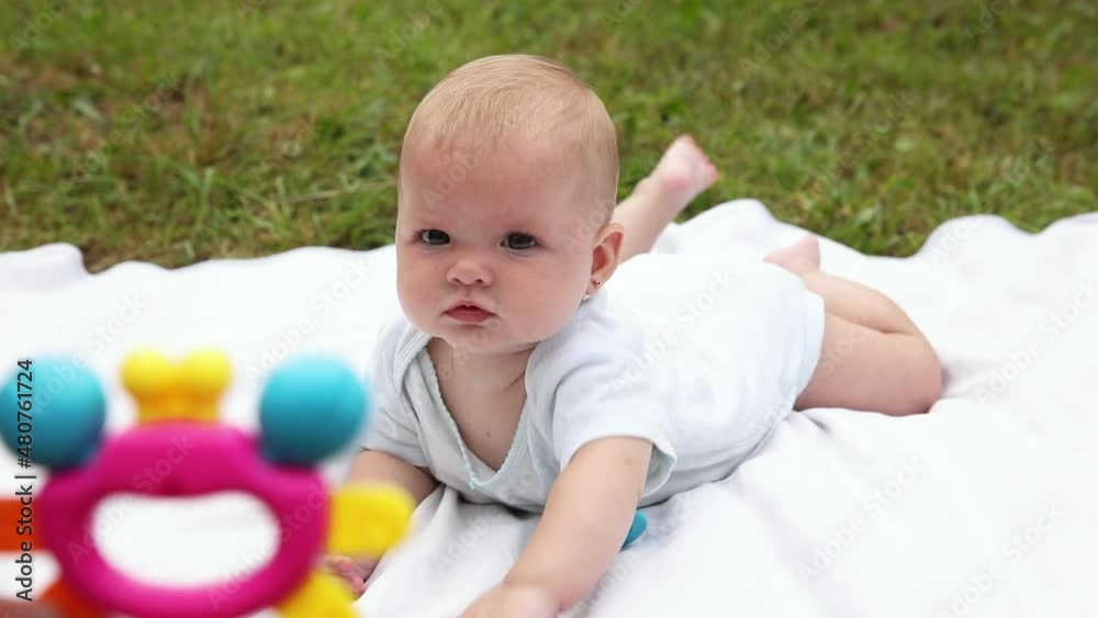 Cute little newborn girl lying on tummy on blanket in lawn on sunny summer day outdoor. Infant having fun outdoors. Infant baby child resting playing learning to crawl. Motherhood happy child concept Cute little newborn girl lying on tummy on blanket in lawn on sunny summer day outdoor. Infant having fun outdoors. Infant baby child resting playing learning to crawl. Motherhood happy child concept