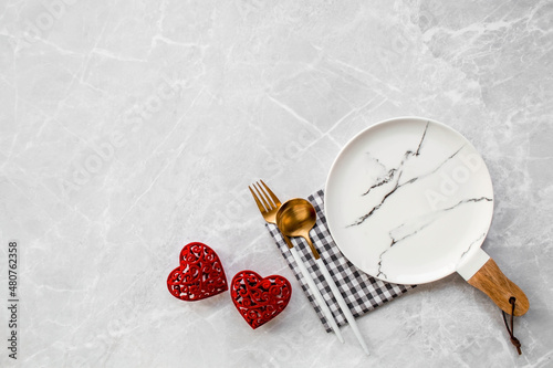 Banner. Table setting. A fashionable marble plate with a napkin, fork and red hearts on a gray background. Valentine's Day holiday concept for cafes and restaurants. A copy of the place for the text.