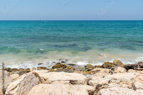 Turquoise water crashing onto brown rocky shore with blue sky