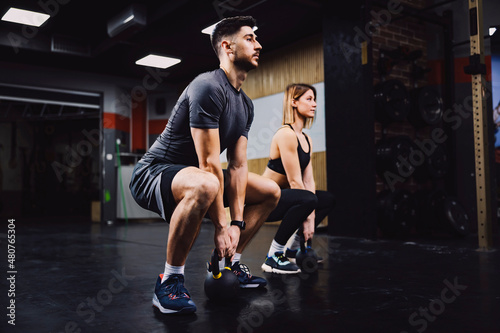 A fitness couple doing powerlift exercises with kettlebells in a gym.