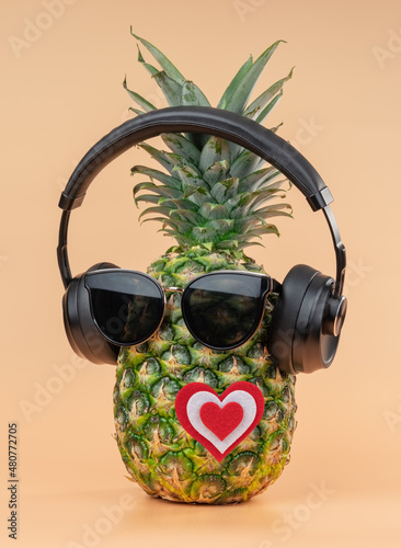 The idea of lovers for valentine's day in the image of a pineapple wearing headphones and sunglasses. On a yellow background.