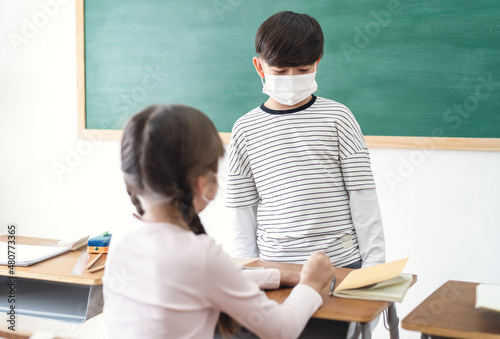 Elementary school kids wearing medical face masks talking during lesson in classroom. Conversation before class. Back to school after covid-19 quarantine.