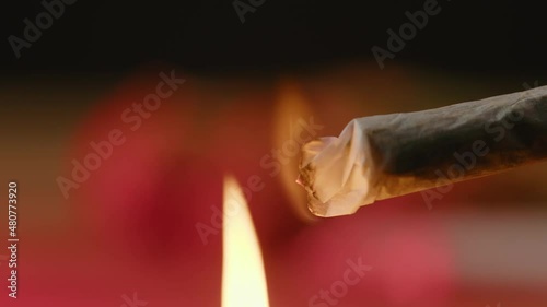 Flame lighting up a rolled marijuana joint on a background with blinking, red and blue lights, close-up shot. photo