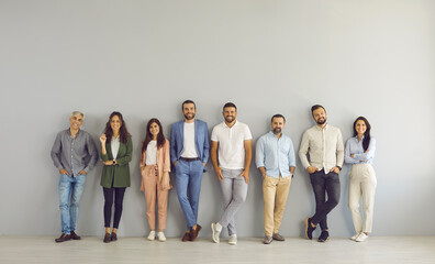 Full body portrait of happy business people in smart and casual clothes. Full length group of senior and young Caucasian men and women posing against grey studio wall. Clothing and fashion concept