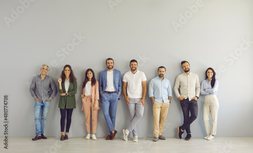 Full body portrait of happy business people in smart and casual clothes. Full length group of senior and young Caucasian men and women posing against grey studio wall. Clothing and fashion concept photo