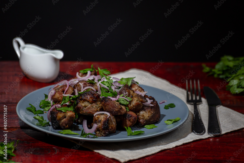 Shashalyk - pieces of pork fried over charcoal with shallots, sauce and herbs on a slate tray with a dark background.