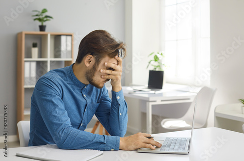 Tired man has a burnout. Stressed office worker or entrepreneur sitting at desk hiding face in hands feeling unwell or overwhelmed with frustration and unable to look at laptop computer screen anymore