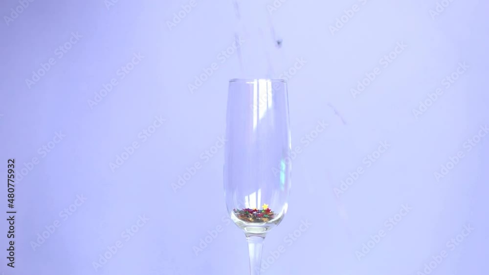 Shiny muilucolor sequins fall down and fill the champagne glass on very peri purple background. holidays Concept