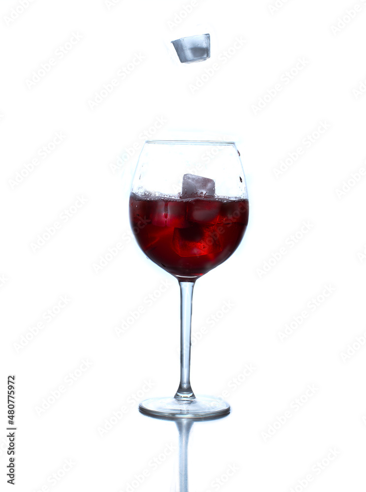 Red soda in a wine glass with ice cubes on the white background. Ice cubes are falling from above to the wine glass. One of them is frozen in the flight.