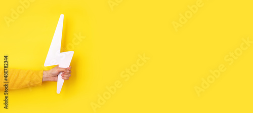 hand holding lightning bolt over yellow background, panoramic layout photo