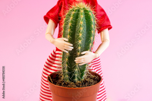 Woman doll hugs a cactus plant on light pink background. Harmful, painful and toxic relationship, partner problems, emotional abuse concept.