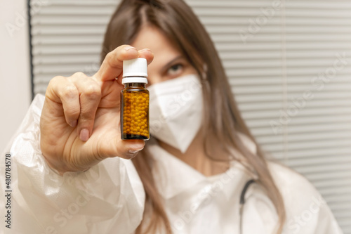 A young doctor wearing a mask holds a glass packet of medicine. A homeopathic medicine. Homeopathic treatment.