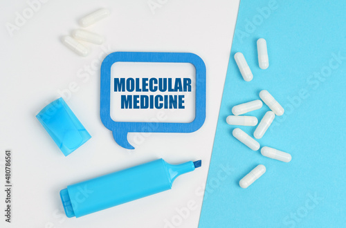 On a white and blue table are pills, a marker and a blue plaque with the inscription - Molecular Medicine