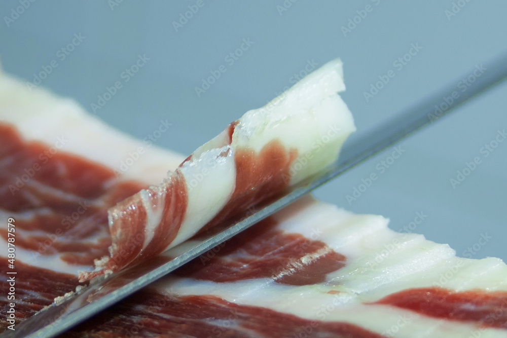 Traditional Spanish food ham Serrano, sliced special long knife close-up. Stock Photo | Adobe