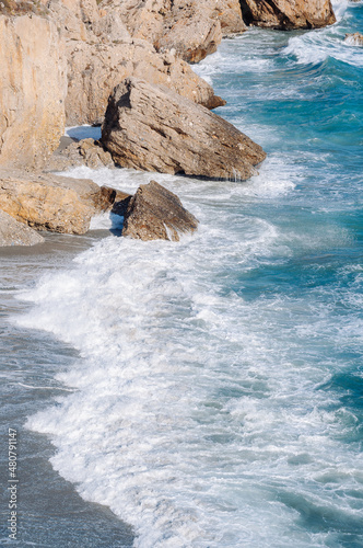 Aerial top view of sea waves hitting rocks on the beach with turquoise sea water. 