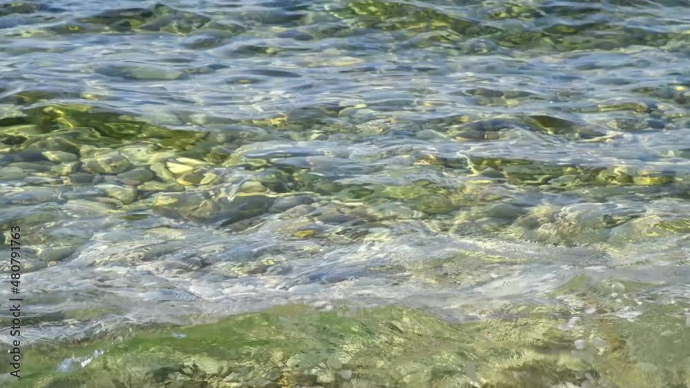 Selective focus. Close-up view of small waves on transparent light green sea water pebble beach on a sunny day. 4K resolution video. Sea resort theme. Selective focus. Close-up view of small waves on transparent light green sea water pebble beach on a sunny day. 4K resolution video. Sea resort theme.