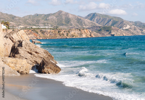 Aerial top view of sea waves hitting rocks on the beach with turquoise sea water. 