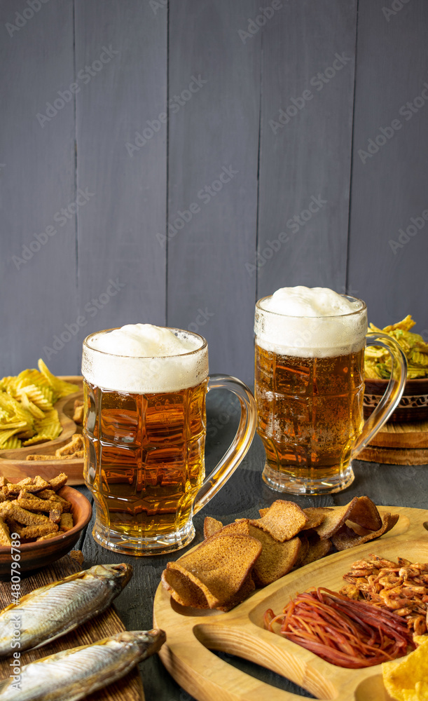 Mugs of cold beer with foam served on a wooden table with salty snacks in a wooden bowl
Mugs of cold beer with foam served on a wooden table with salty snacks in a wooden bowl