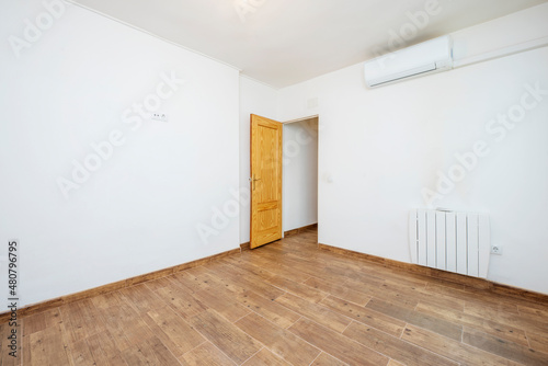 Freshly painted empty room with dark wood tile floor and pine wood door  white air conditioner and radiator